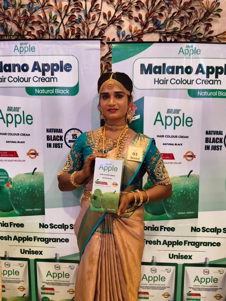 Exhibition participant holding Malano Apple hair colour cream product during booth presentation