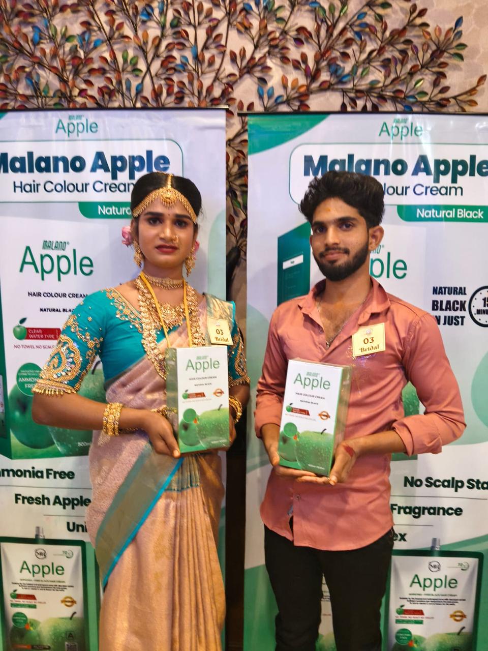 Two exhibition participants holding Malano Apple hair colour cream products at the PRIIS display